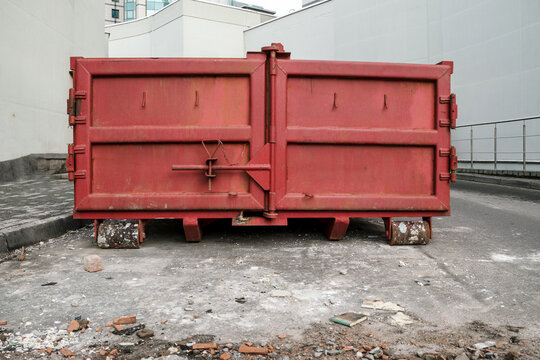 huge red metal garbage container between light walls of large buildings on backstreet