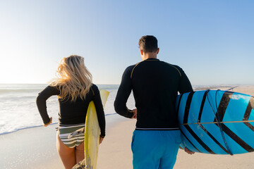 Caucasian couple holding surfboards at the beach.