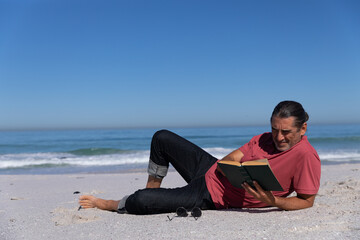 Fototapeta na wymiar Senior Caucasian man reading a book at the beach.