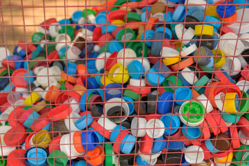 Lids from plastic bottles in a mesh container. Different colors. Selective focus. Concept of separate collection of waste, environmental recycling and disposal.