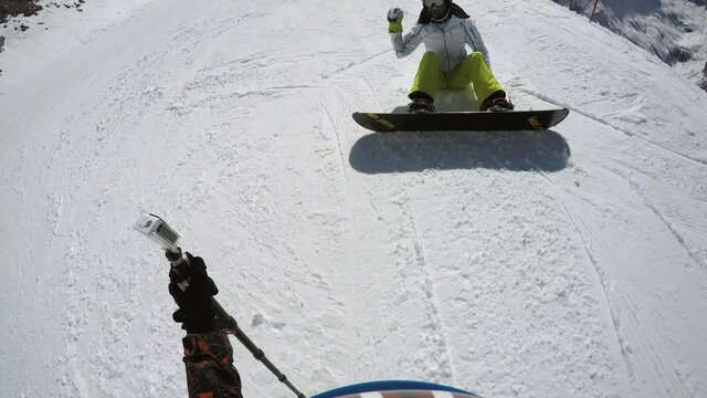 FPV snowboarder sitting on slope throws snow at action camera on monopod