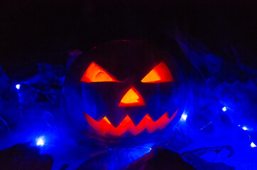 Orange pumpkin with glowing eyes, mouth in the dark in blue lighting in the smoke close-up. concept of Halloween.