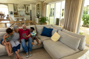 Senior mixed race couple sitting on the couch with their young grandson and granddaughter