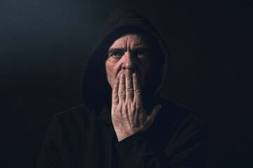 portrait of a man with a hoodie holding a hand in front of his mouth