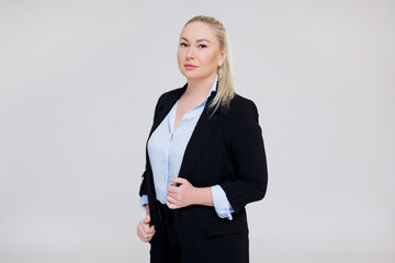 portrait of beautiful plus size blonde woman in black business suit posing over gray background