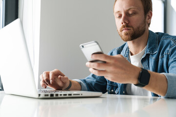 Photo of serious man using cellphone and laptop while sitting at table