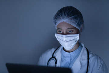 Healthcare worker wearing face mask during coronavirus Covid19 pandemic and using laptop