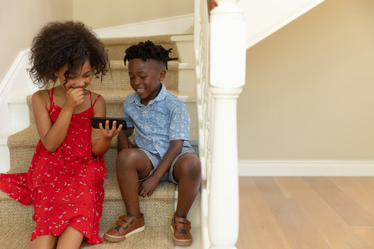 Mixed race girl and her younger brother using phone at home