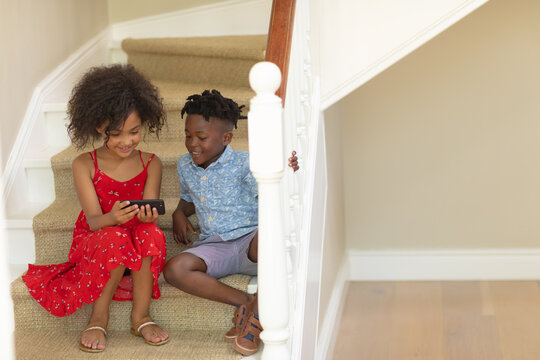 Mixed race girl and her younger brother using phone at home