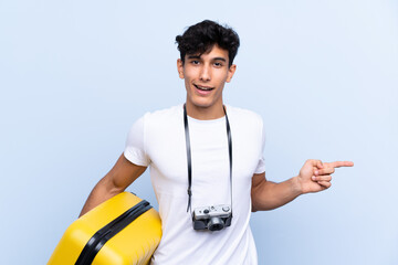 Young Argentinian traveller man over isolated blue background surprised and pointing finger to the...
