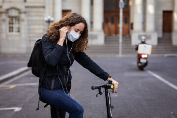 Caucasian woman wearing a protective mask on her bike, wearing earphones in the streets