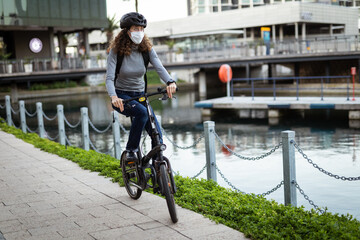Fototapeta premium Caucasian woman wearing a protective mask and a cycling helmet in the streets, biking in the streets