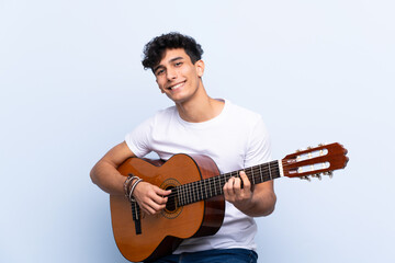 Obraz premium Young Argentinian man with guitar over isolated blue background surprised and pointing finger to the side