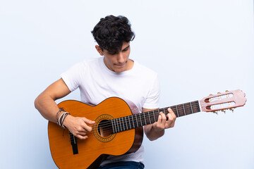 Young Argentinian man with guitar over isolated blue background