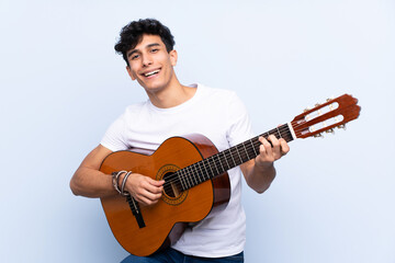 Young Argentinian man with guitar over isolated blue background