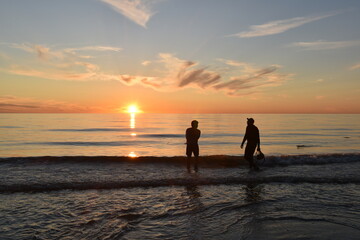 Katwijk aan Zee / The Netherland - June 20 2020: Local sports fishermen are walking in the sea, trawling their fishnet along the beach fishing for sole, in the evening at sun set. 