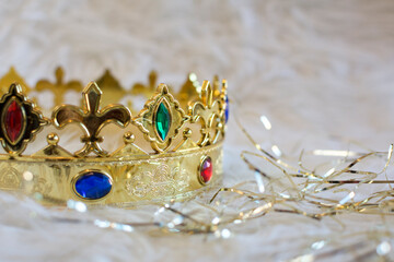 Royal gold crown, with colored gems and diamonds, on a white background with golden bands surrounding it.