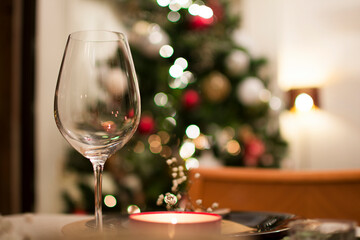A crystal wine glass close-up on the table, with the bokeh of Christmas tree lights behind.