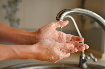 
Washing hands with soap near the tap. Water pours from the tap.