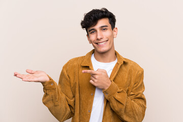 Young Argentinian man over isolated background holding copyspace imaginary on the palm to insert an...