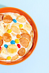 Orange bowl with tiny pancake cereal porridge with milk on a blue background top view close-up.Trendy tasty breakfast food