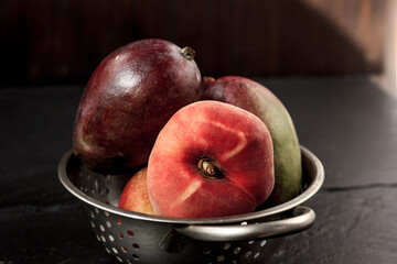 Mango and peach fruits in metal colander