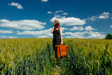Naklejka na ściany i meble Beautiful blonde girl with suitcase and vintage camera in wheat field in sunny day
