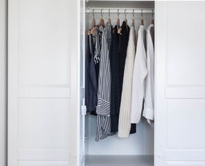 Fashion stylist clothes basic wardrobe.Neutral colors: white, black, beige. White closet, wooden hanger shoulders.