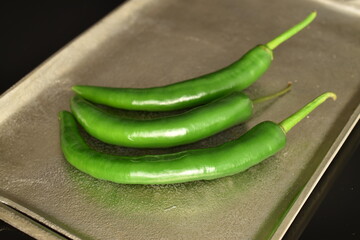 Green chili peppers on a metal tray, on a black background.