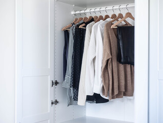 Fashion stylist clothes basic wardrobe.Neutral colors: white, black, beige. White closet, wooden hanger shoulders.