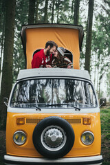 Traveler couple embracing and resting in forest on Orange retro Bulli Vintage Camper.
