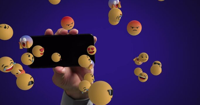 Hand holding smartphone with emoticons spawning
