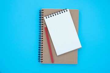 Top view above of open blank spiral notebook and red pencil isolated on light blue background for design mockup. Education and business concept. flat lay