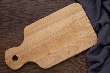 Top view above of Wooden chopping board with napkin on dark table background. Wood Cutting board with handle and hole for hanging. Empty utensil with copy space.