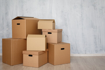 moving day or postal delivery concept - brown cardboard boxes stacked on the floor and copy space over gray wall