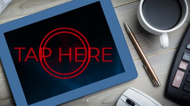 Animation of red words Tap Here flickering on screen of digital tablet put on a desk with cup of cof