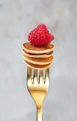 Tiny cereal pancakes with raspberries strung on a fork on a dark background