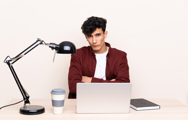 Young Argentinian man in a table with a laptop in his workplace sad