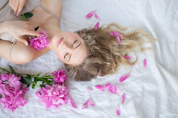 Obraz na płótnie Canvas beautiful sensual girl with long blonde hair in dress with a bouquet of pink peonies flowers. Close-up portrait of a woman in studio on a gray white background.concept of feminity spa