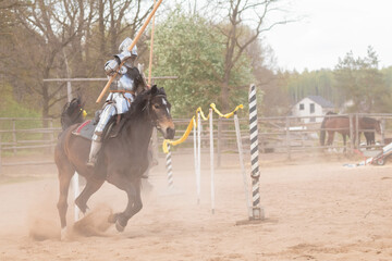 A knight in vintage armor of the 15th century rides a horse across a field for a tournament