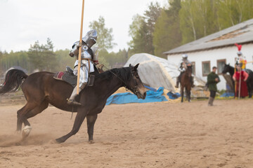 A knight in vintage armor of the 15th century rides a horse across a field for a tournament