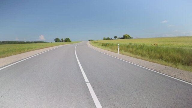 Winding asphalt road in Latvia. Along the edges sown fields of argo with cereals to the horizon. Red poppies on the sidelines. Camera Lift Over Lane. Baltic state