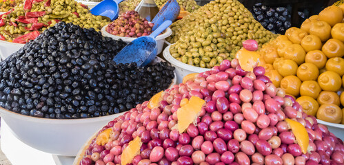 Mounts of red, black, and green olives with blue scoopers in white bowls displayed in souk Essaouria, Morocco.