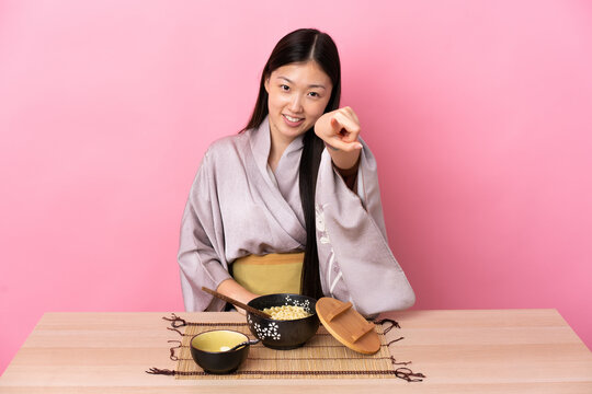 Young Chinese Girl Wearing Kimono And Eating Noodles Pointing Front With Happy Expression