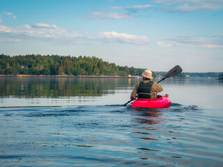 Red kayak paddles on calm water in Maine summer morning
