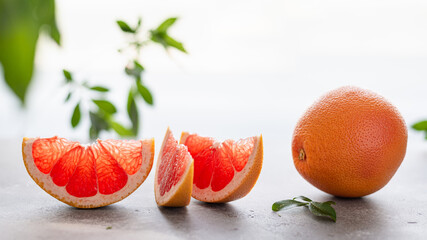 Juicy grapefruit pieces with whole fruit and green leaves on white background. close up, copy space. Superfoods, dieting, vitamins