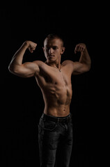 Fototapeta na wymiar Young attractive bodybuilder with a naked torso poses for the photographer on a black background.