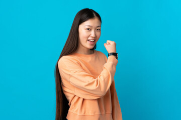 Young Chinese girl over isolated blue background celebrating a victory