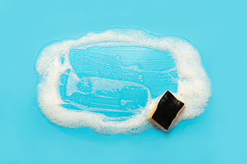 Soap foam from a cleaning agent and a cleaning sponge on a blue background. Cleaning concept,...