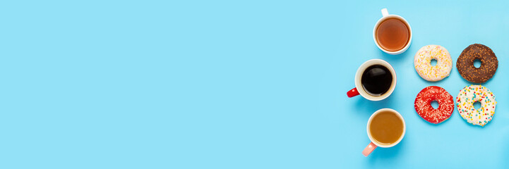 Tasty donuts and cups with hot drinks, coffee, cappuccino, tea on a blue background. Concept of sweets, bakery, pastries, coffee shop, meeting, friends, friendly team. Banner. Flat lay, top view